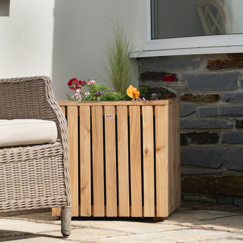 Premium Cedar Slatted Panel Planter shown in garden setting with plants, displaying the elegant vertical slatted design, square 500mm profile, and the natural cedar finish that weathers beautifully outdoors 